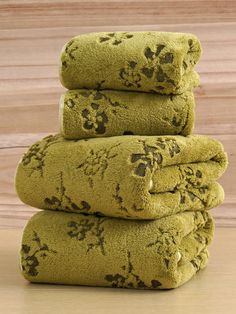 a stack of four green towels sitting on top of a wooden table next to a wall