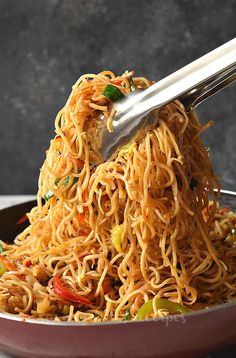 a bowl full of noodles and vegetables with tongs sticking out of the top, ready to be eaten