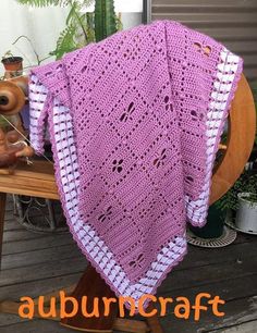 a pink crocheted blanket sitting on top of a wooden table next to a potted plant