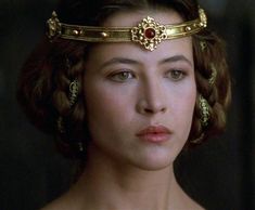 the young woman is wearing a gold headpiece with red stones on it's forehead