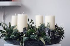 four candles are sitting on a table with greenery