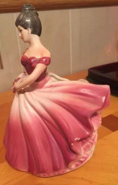 a ceramic figurine of a woman in a pink dress sitting on a table