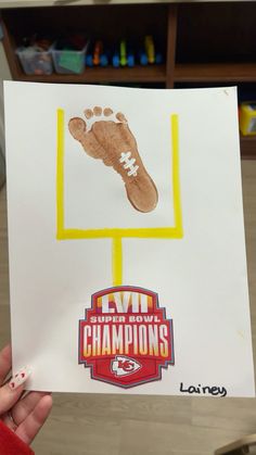 a hand holding up a paper with a drawing of a football trophy and foot print on it