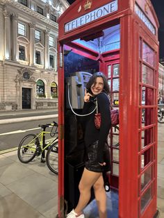 a woman standing in a red phone booth