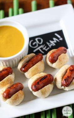 small hot dogs on buns with mustard and dipping sauce in a white bowl sitting on a plate