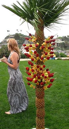 a woman standing next to a tall palm tree with fruit on it's trunk