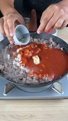 a person pouring sauce into a pan filled with food