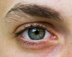 a man's blue eye is seen from the bottom up, with brown hair on his head