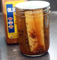 a jar filled with pickles sitting on top of a counter next to a bottle