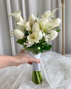 a bouquet of white flowers is held by a woman's hand on a bed