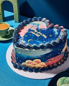 there is a blue cake with stars and moon decorations on the table next to some cupcakes