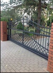 an iron gate with brick pillars on the side of a sidewalk in front of a tree