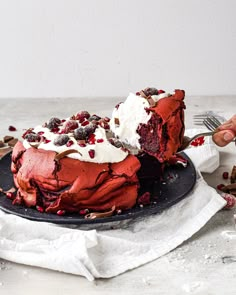 a red velvet cake with white frosting and sprinkles on a black plate