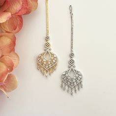 two pairs of dangling earrings on a white surface with flowers in the foreground and behind them is a pink flower