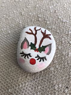 a rock painted to look like a reindeer's nose with holly leaves on it