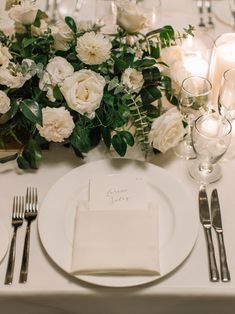 the table is set with white flowers and silverware, candles, and napkins