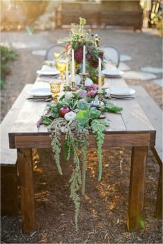 a long wooden table topped with lots of flowers and greenery on top of it