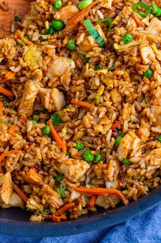 a bowl filled with rice and vegetables on top of a blue cloth next to a wooden spoon