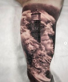 a man's leg with a lighthouse tattoo on it and clouds in the sky