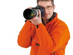 a man in an orange jacket is taking a photo with a large lens on his camera