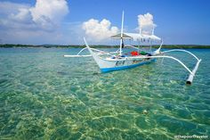 a boat floating on top of the ocean next to a shore line under a blue sky