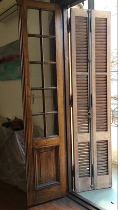 an open wooden door with shutters on the inside and outside, in front of a bed