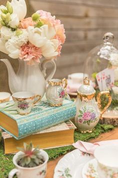 a table topped with books and vases filled with flowers next to teapots