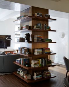 a living room filled with lots of books on top of wooden shelves next to a gray couch