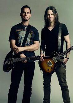 two men standing next to each other with guitars in their hands and one holding an electric guitar