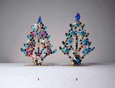 two pairs of colorful crystal earrings sitting on top of a white table next to each other