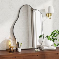 a mirror sitting on top of a wooden dresser next to a vase and potted plant