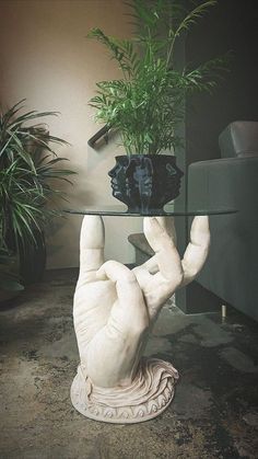 a glass table topped with a plant and a hand holding it up in the air