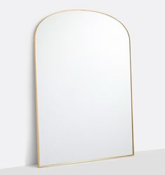 a white mirror sitting on top of a counter next to a wall mounted shelf with a gold frame