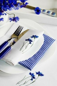 a white plate topped with blue flowers next to a fork and knife on top of a table