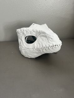 a white vase sitting on top of a table next to a gray wall with a hole in it