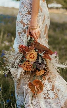 a woman in a white dress holding a bouquet with feathers and flowers on the grass