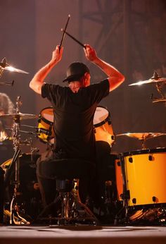 a man sitting on top of a drum set with his hands up in the air