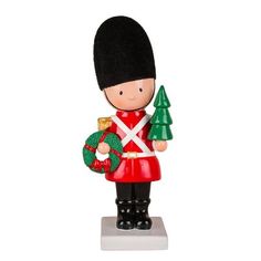 a toy soldier holding a christmas tree and a green ornament on a white background