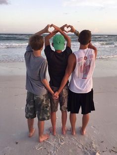 three boys standing on the beach making a heart with their hands