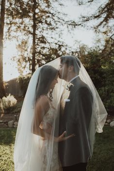 a bride and groom standing under a veil in the grass at their outdoor wedding ceremony