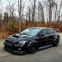 a black subarunt is parked on the side of the road in front of some trees