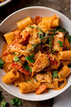 pasta with chicken and tomato sauce in a white bowl on top of a wooden table