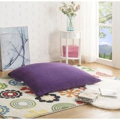 a large purple pillow sitting on top of a white rug next to a painting and chair