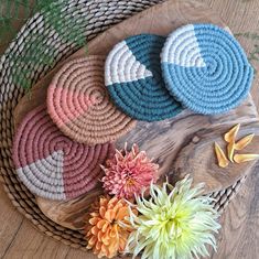 four woven coasters sitting on top of a wooden table next to flowers and leaves