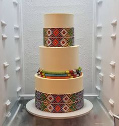 a three tiered cake with beaded decorations on it's sides, in front of a white wall