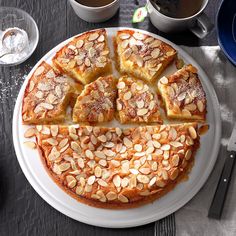 a cake with almonds cut into slices on a plate next to cups of coffee