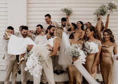 a group of people standing next to each other in front of a white wall holding bouquets