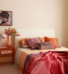 a bed with pink and orange pillows in a bedroom next to a painting on the wall