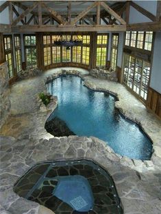 an indoor swimming pool in the middle of a room with large windows and stone flooring