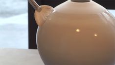 a white vase sitting on top of a table next to a glass window with a wooden spoon sticking out of it